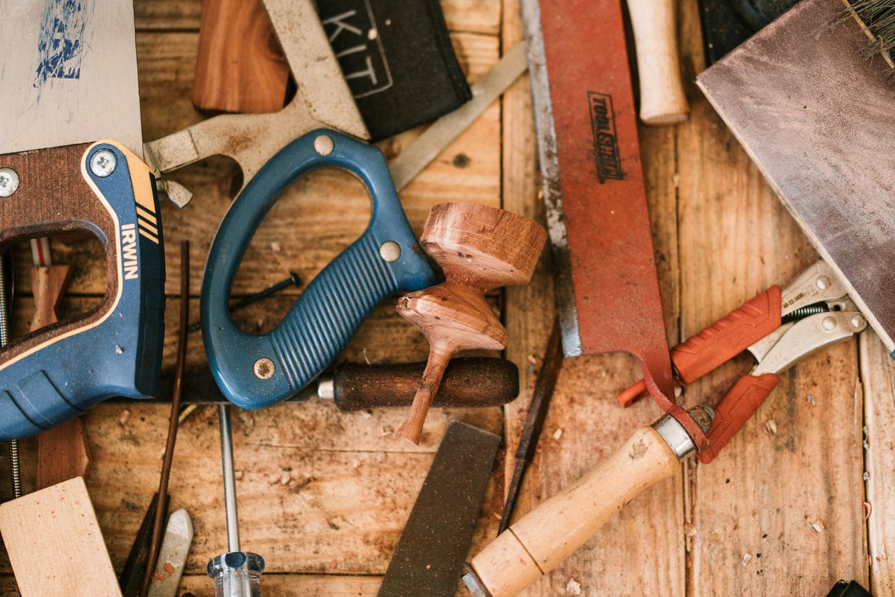 Hand saws, clamps, chisels and a wood plane laid out on a carpenter's workbench